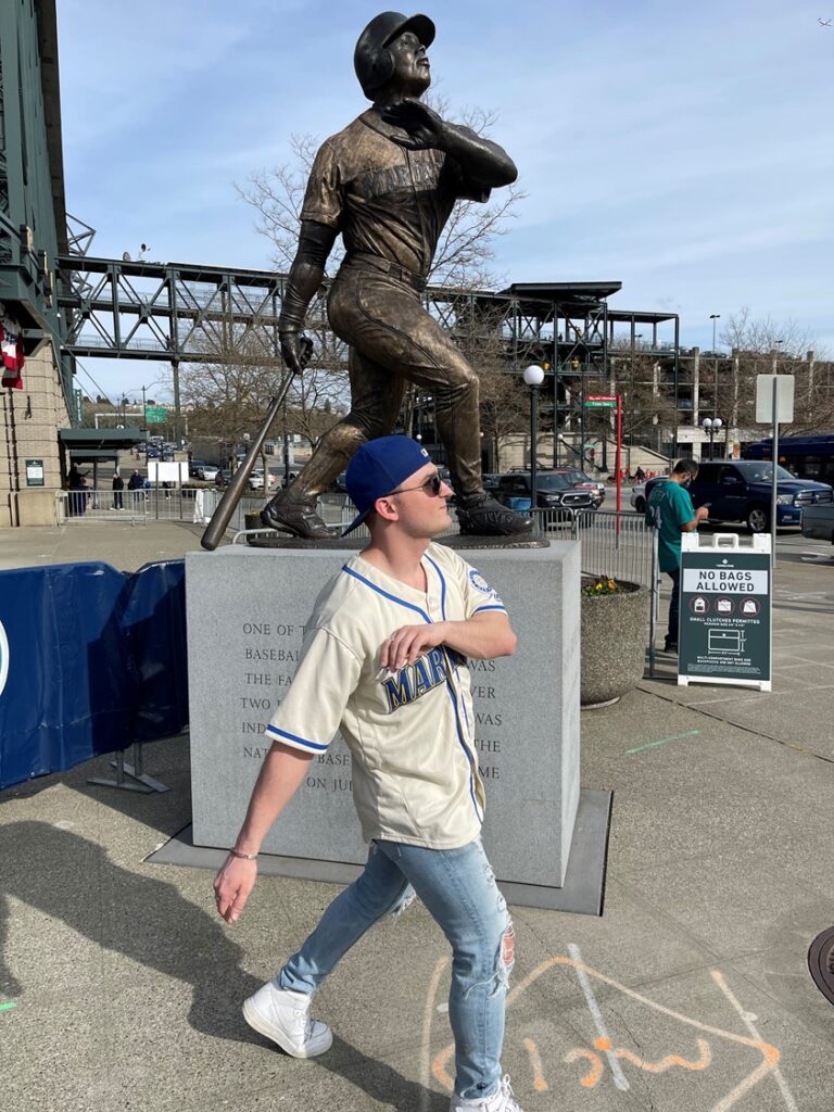 A man wearing a white top and blue cap while imitating the position of the statue